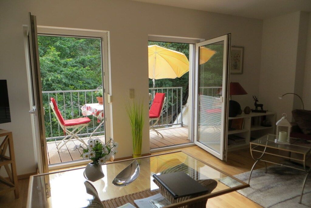 A room with a glass table, a red chair, a yellow umbrella, and a view of a balcony with a red chair and a table.