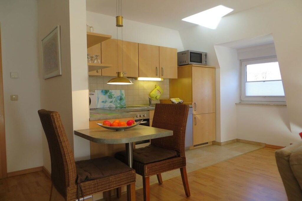 A compact kitchen with wooden cabinets, a dining table with chairs, a microwave above the stove, and a window providing natural light.