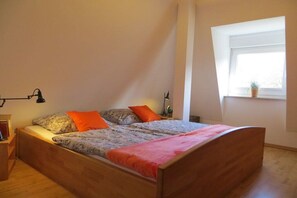 Un dormitorio con una cama de madera, una mesita de noche, una lámpara y una ventana con una planta.
