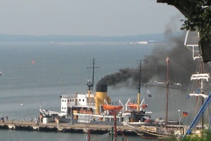 A ship with a smokestack emitting black smoke, docked at a pier with other boats and a lifeboat visible. - A holiday with only a sea view (Sassnitz)