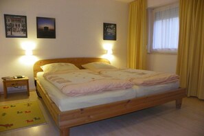 A single-bed room with a wooden frame, two bedside lamps, a nightstand, a window with yellow curtains, and two wall-mounted pictures. - A holiday with only a sea view (Sassnitz)