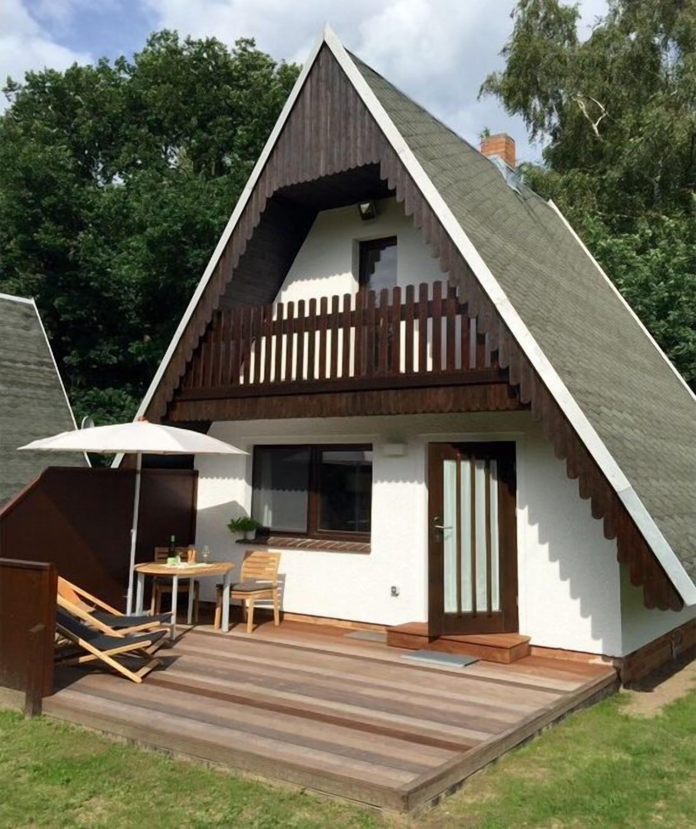 A triangular house with a wooden deck, a small table with chairs, and a door.