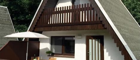A triangular house with a wooden deck, a small table with chairs, and a door.