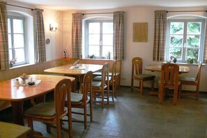 A dining area with wooden tables and chairs, large windows with curtains, and a tiled floor. - Zum Grünen Hirsch Stolln (Breitenbrunn OT Rittersgrün)
