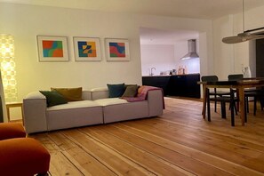 A living room with a sofa, a dining table with chairs, and a kitchen in the background. - Apartment in Görlitz with swimming pool (Görlitz)