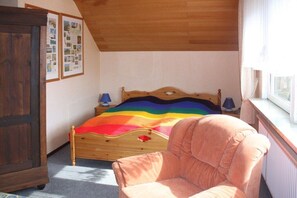 Een slaapkamer met een houten bed, een roze stoel, een raam en een deur.