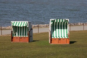 Two beach chairs with striped covers, positioned on a grassy area near a body of water. - Holiday home with 3 bedrooms (Nordstrand)
