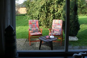 Two chairs with patterned upholstery facing a window, a small table with a pink object, and a view of a green garden. - Holiday home with 3 bedrooms (Nordstrand)