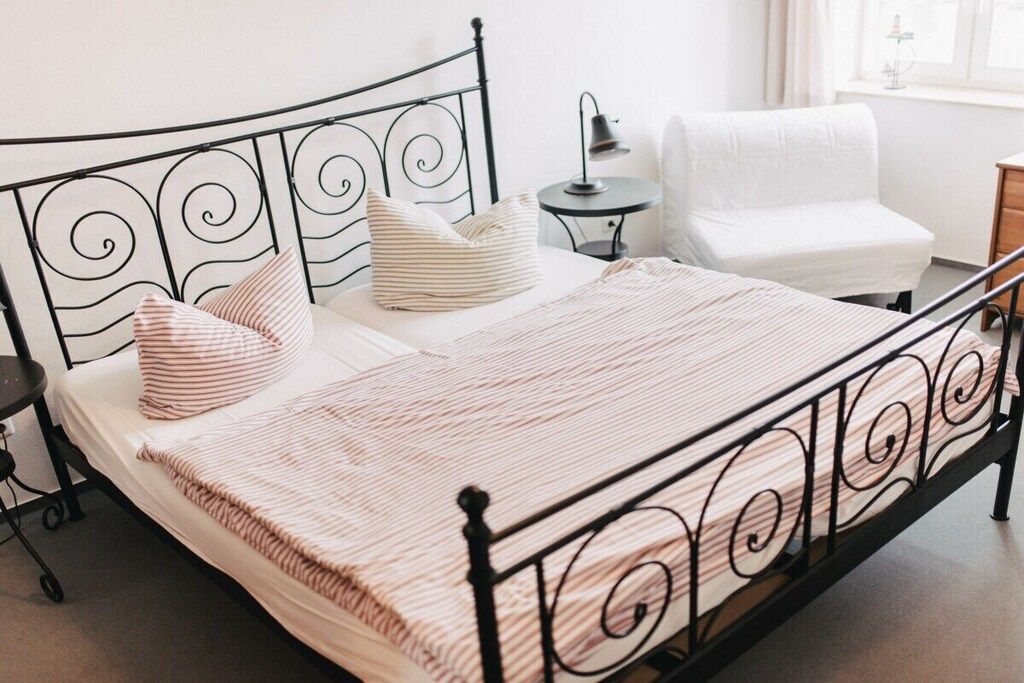 Ein Bett mit Metallgestell, ein Nachttisch, eine Lampe und ein Stuhl.