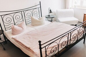 Uma cama com estrutura metálica, uma mesinha de cabeceira, uma luminária e uma cadeira.