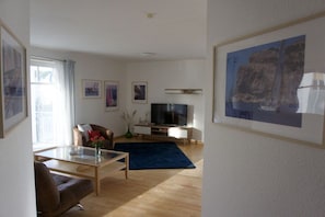 Ein modernes Wohnzimmer mit Fernseher, Sofa, Couchtisch und Kunstwerken an den Wänden.