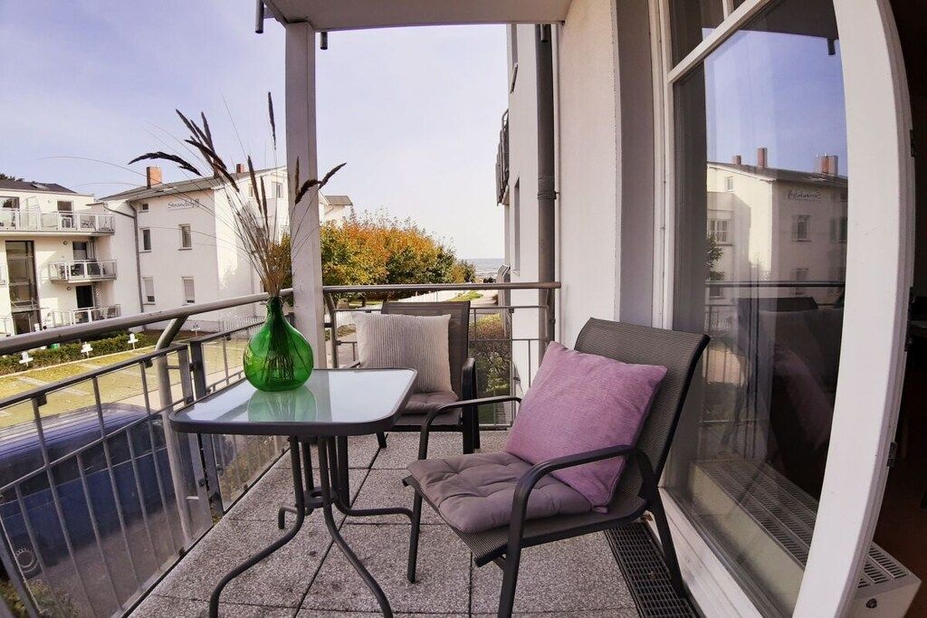 A balcony with a table and chairs, a green vase, and a view of buildings and trees.