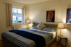 Ein Hotelzimmer mit Bett, zwei Nachttischlampen, einem Fenster mit Vorhängen und einem Bild an der Wand.