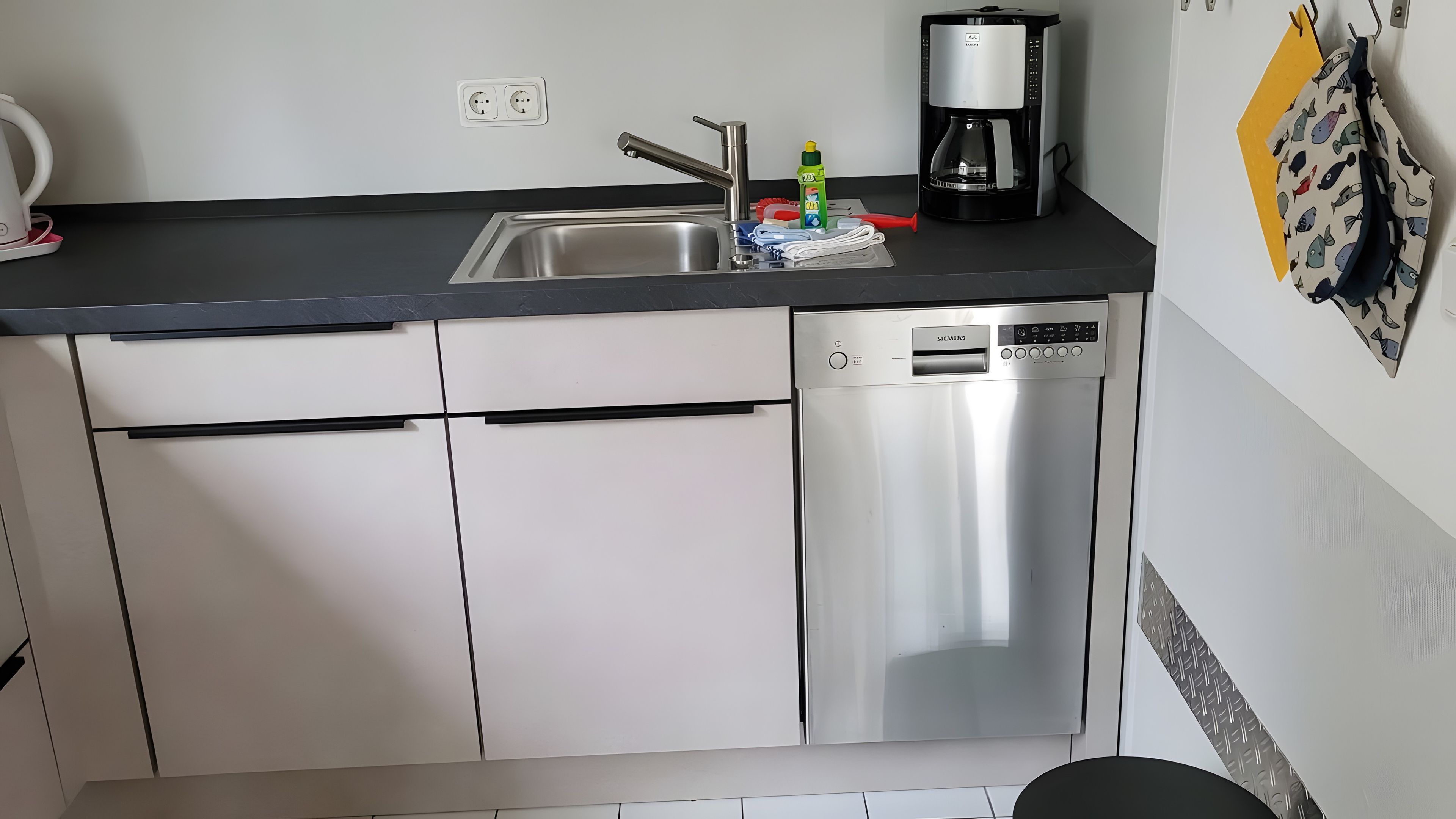 Eine Küche mit einem Edelstahl-Geschirrspüler, einer Kaffeemaschine und einem Spülbecken.