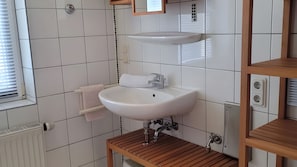 Ein Badezimmer mit einem weißen Waschbecken, einem Holz-Waschtisch und einem Fenster mit Jalousien.