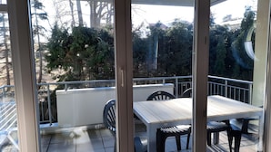 A balcony with a table and chairs, overlooking a garden with trees and a building in the background. - Apartment 'Zinnowitz, Dünenstraße WE 15' with Balcony and Wi-Fi (Zinnowitz)
