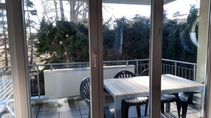 Ein Balkon mit Tisch und Stühlen, mit Blick auf einen Garten mit Bäumen und einem Gebäude im Hintergrund.