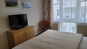 Ein Hotelzimmer mit einem Bett, einem Fernseher auf einer Holzkommode, einem Sessel und zwei Bildern an der Wand.