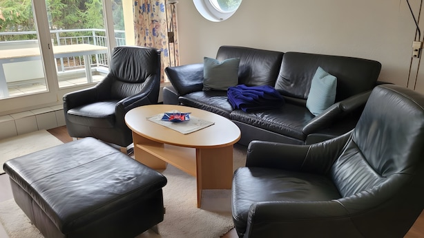 A modern living room with a leather sofa, two armchairs, a coffee table, and a view of the outdoors through large windows. - Apartment 'Zinnowitz, Dünenstraße WE 15' with Balcony and Wi-Fi (Zinnowitz)