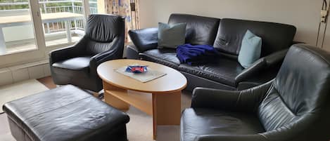 A modern living room with a black leather sofa, two armchairs, and a round coffee table.