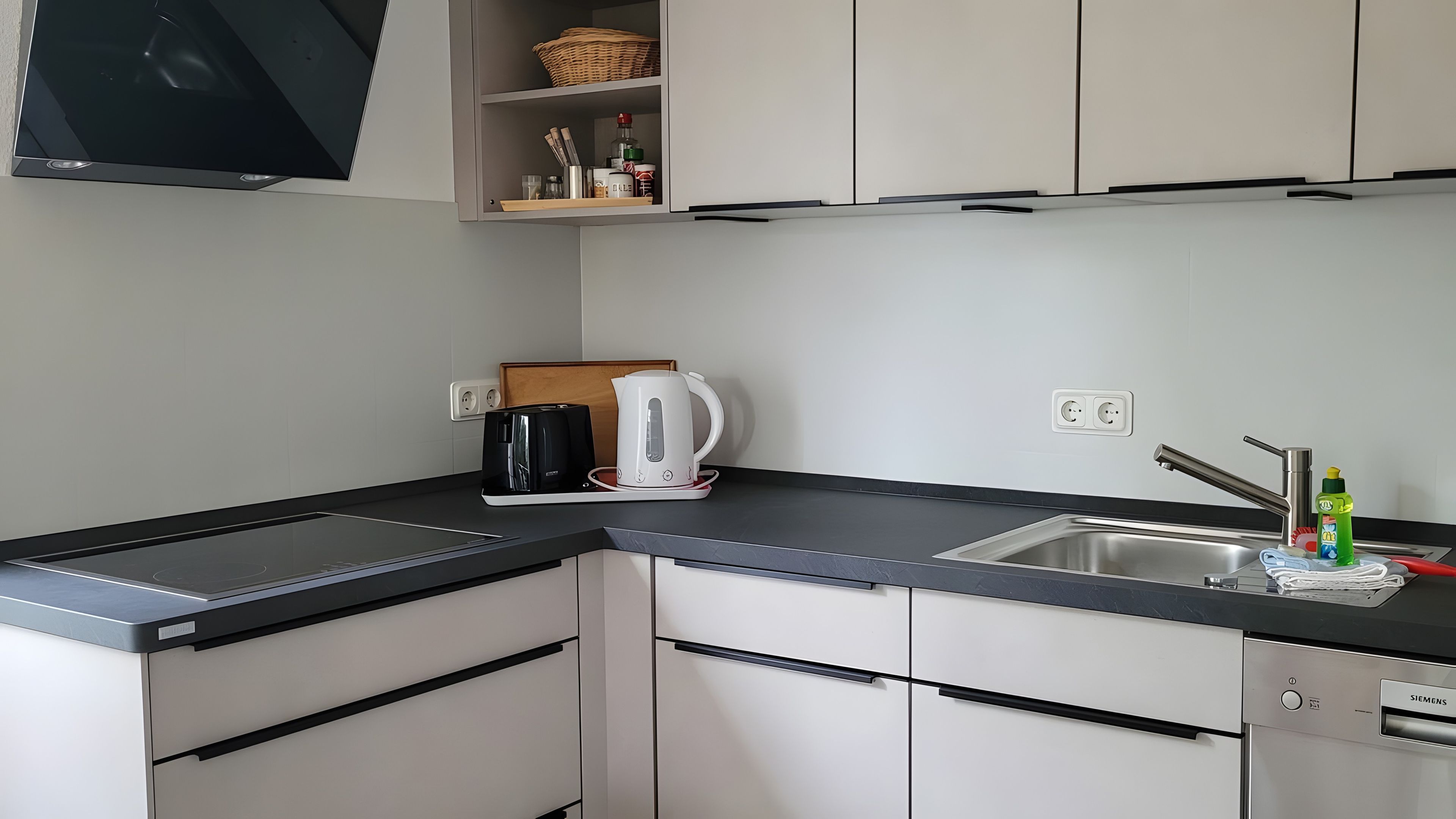 Una cocina moderna con encimera negra, armarios blancos, una tetera, una cafetera y un lavavajillas Siemens.