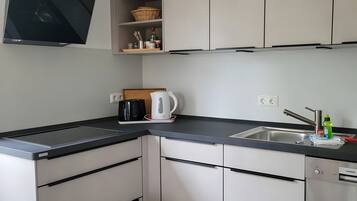 Una cocina moderna con encimera negra, armarios blancos, una tetera, una cafetera y un lavavajillas Siemens.