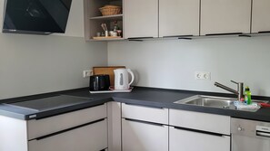Eine moderne Küche mit schwarzem Arbeitsplatz, weißen Schränken, einem Wasserkocher, einer Kaffeemaschine und einem Siemens Geschirrspüler.