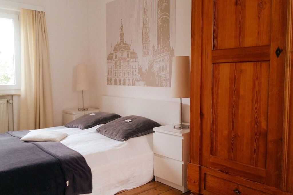 Habitació d'hotel amb un llit, dues làmpades de nit, un armari de fusta i una finestra amb cortines.