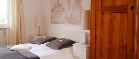 A hotel room with a bed, two bedside lamps, a wooden wardrobe, and a window with curtains.
