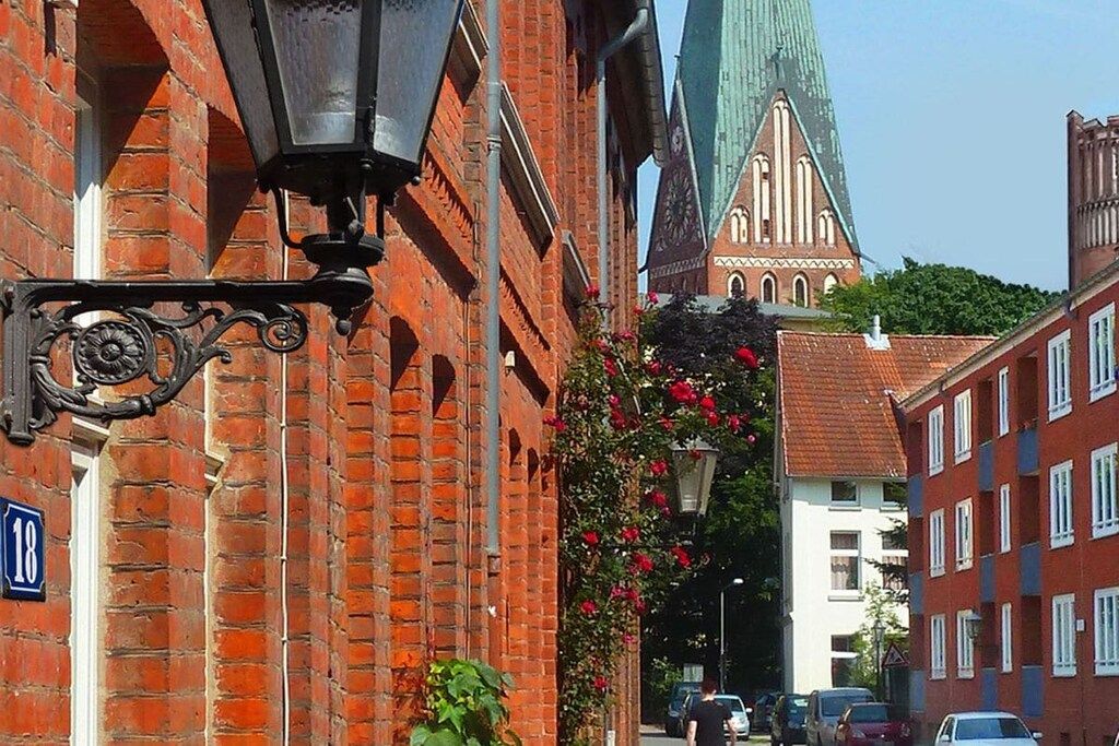 Une rue bordée d’un immeuble en briques rouges, d’une église surmontée d’une flèche verte et d’un lampadaire.