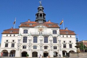 A historic building with a central clock tower, arched windows, and flags. - Holiday apartment with 1 bedroom (Lüneburg)