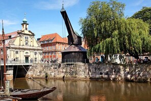 A riverside view with a historic bridge, a church, and a tree-lined walkway. - Holiday apartment with 1 bedroom (Lüneburg)