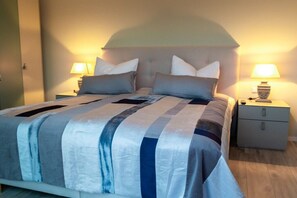 Una cama doble con una colcha a rayas, dos mesitas de noche con lámparas y una mesita de noche con lámpara.