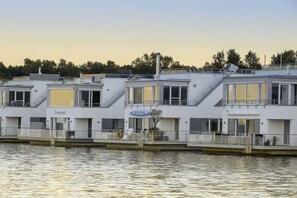 A row of white buildings with balconies, a sign that reads 'Traumzeit,' and a calm water body in the foreground. - Holiday home with 2 bedrooms (Bitterfeld-Wolfen)