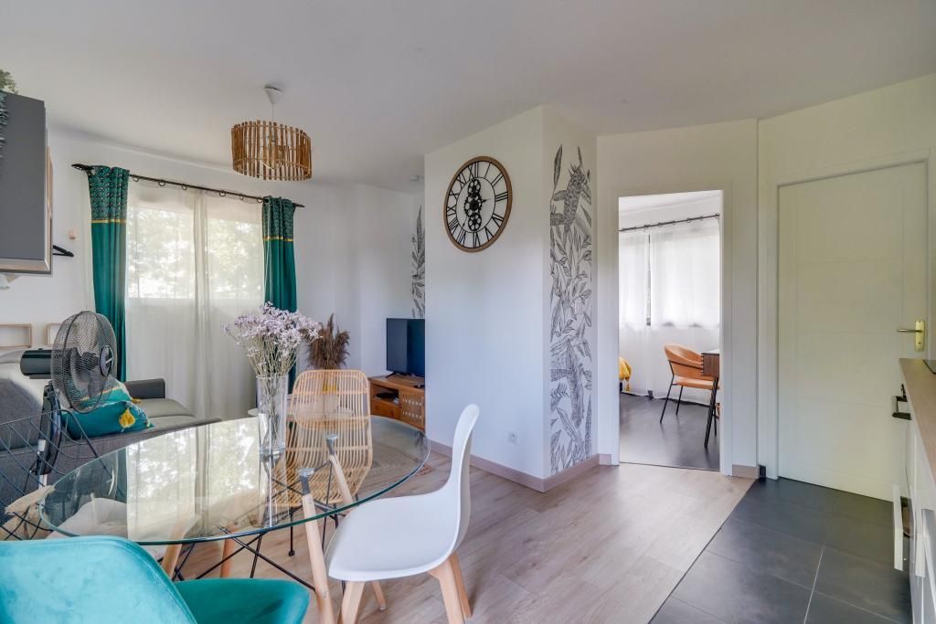 Un salon moderne avec une table à manger en verre, un canapé, un téléviseur et une horloge murale décorative.