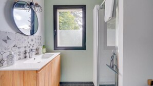 A bathroom with a double sink, wooden cabinets, a round mirror, and a window with a view of trees. - Le Maobi · Quiet 2-bedroom apartment with a terrace and parking, 15 minutes from Bordeaux (Tresses, 33370)