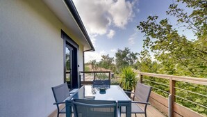 An outdoor patio with a glass table and chairs, a wooden deck, and a view of trees and sky. - Le Maobi · Quiet 2-bedroom apartment with a terrace and parking, 15 minutes from Bordeaux (Tresses, 33370)