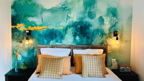 A bed with a white mattress, two pillows, and a yellow blanket. There are two bedside tables with lamps and a radio. - Le Maobi · Quiet 2-bedroom apartment with a terrace and parking, 15 minutes from Bordeaux (Tresses, 33370)