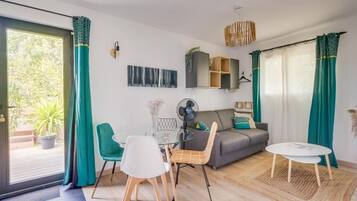 Una sala de estar moderna con una mesa de vidrio, un sofá gris, cortinas verde azulado y vistas a la vegetación.
