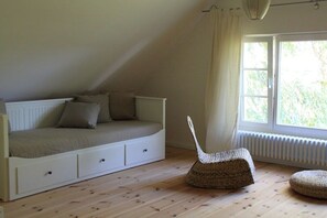 A room with a sloped ceiling, a bed with storage drawers, a woven chair, and a window with curtains. - Holiday home in Usedom with swimming pool (Usedom)