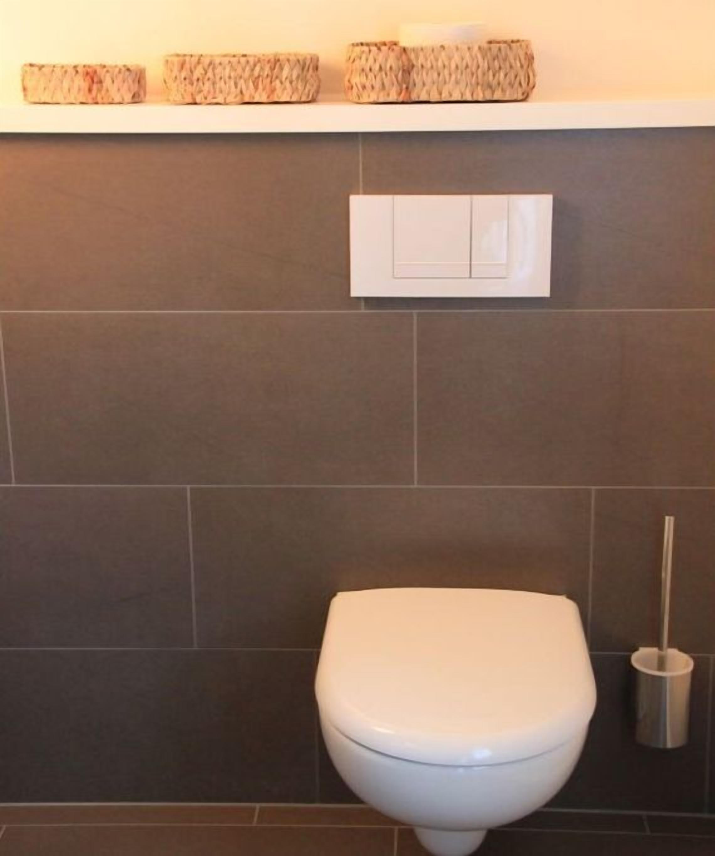 Une salle de bain équipée de toilettes, d'une chasse d'eau murale et d'une brosse pour les toilettes.