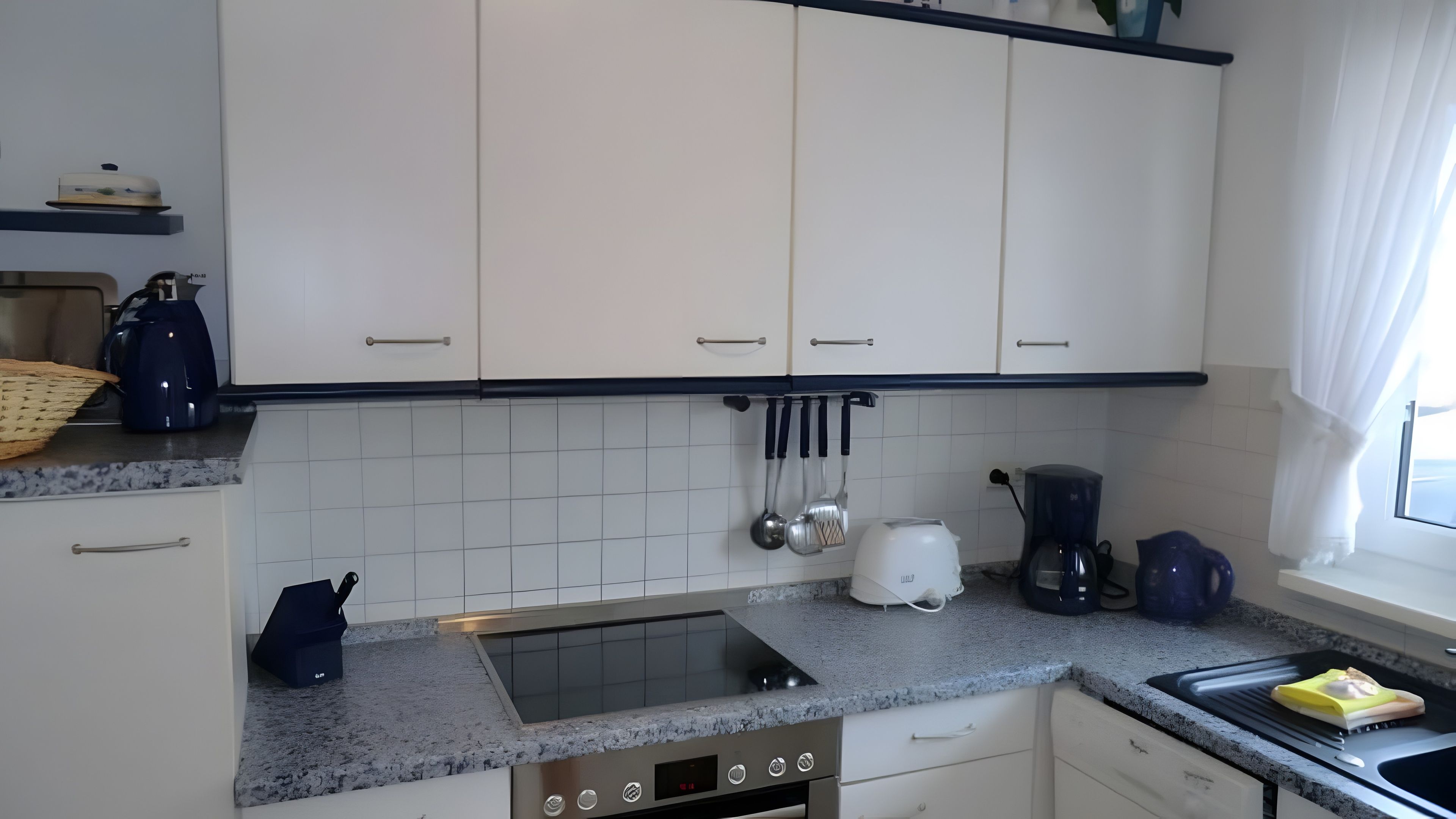 Une cuisine moderne avec des armoires blanches, une cuisinière encastrée et divers appareils, notamment une machine à café et une bouilloire.