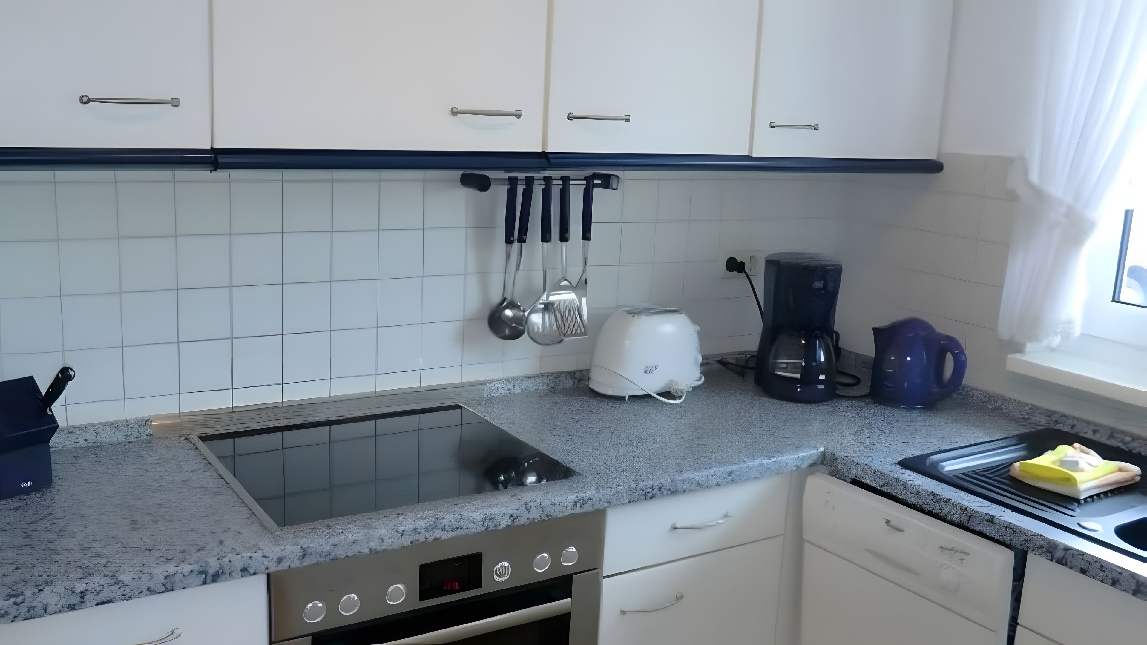 A modern kitchen with white cabinets, a built-in stove, a coffee maker, and a kettle.