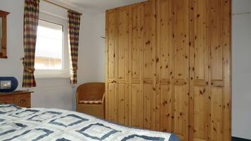 A bedroom with a bed, a wooden wardrobe, a chair, and a window with curtains.