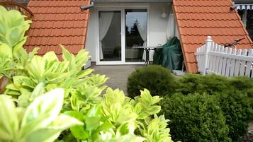 A residential building with a tiled roof, a white picket fence, and a small garden with green shrubs.