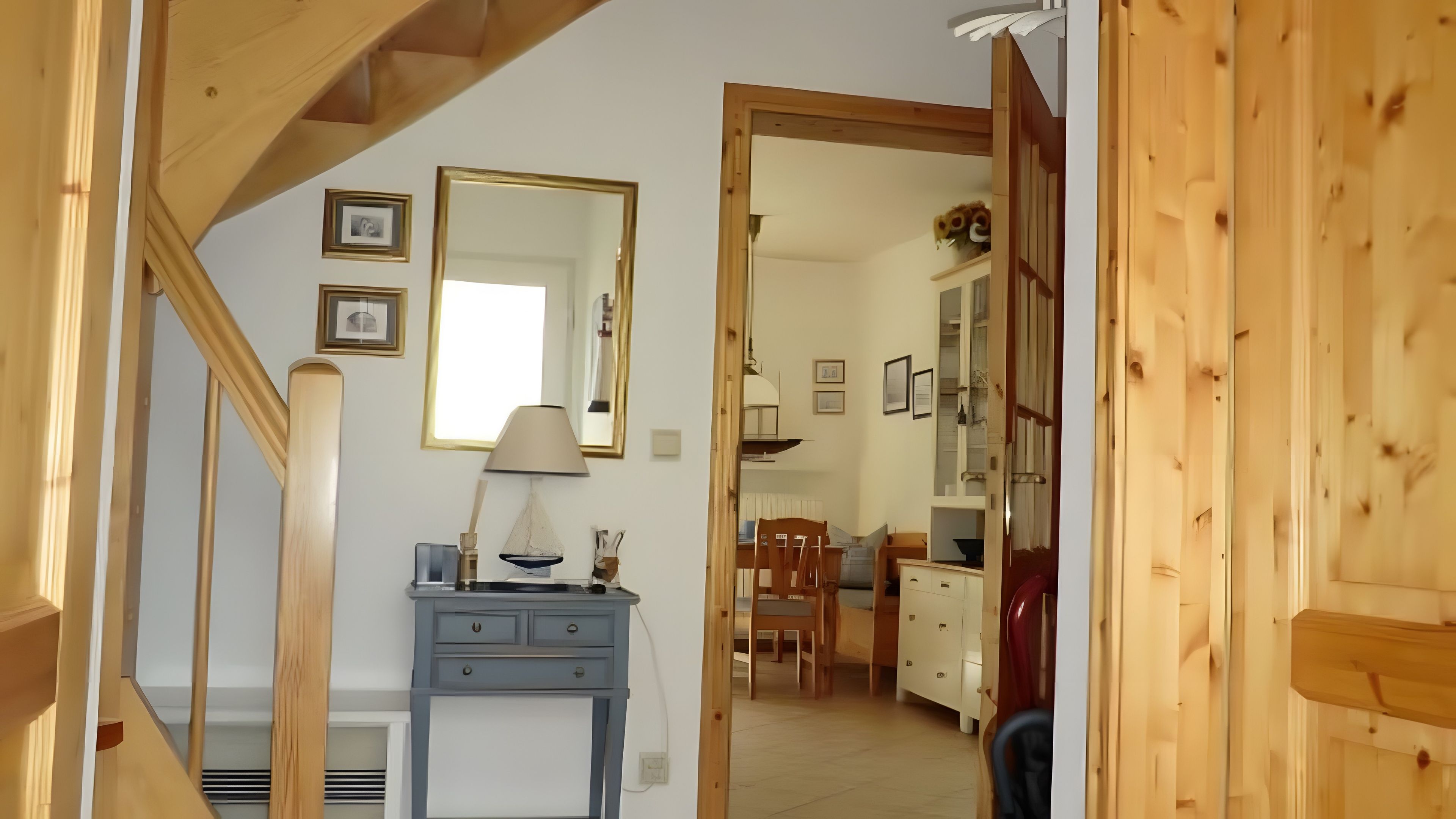 Una escalera conduce a un comedor con una mesa y sillas, un armario azul y un espejo en la pared.