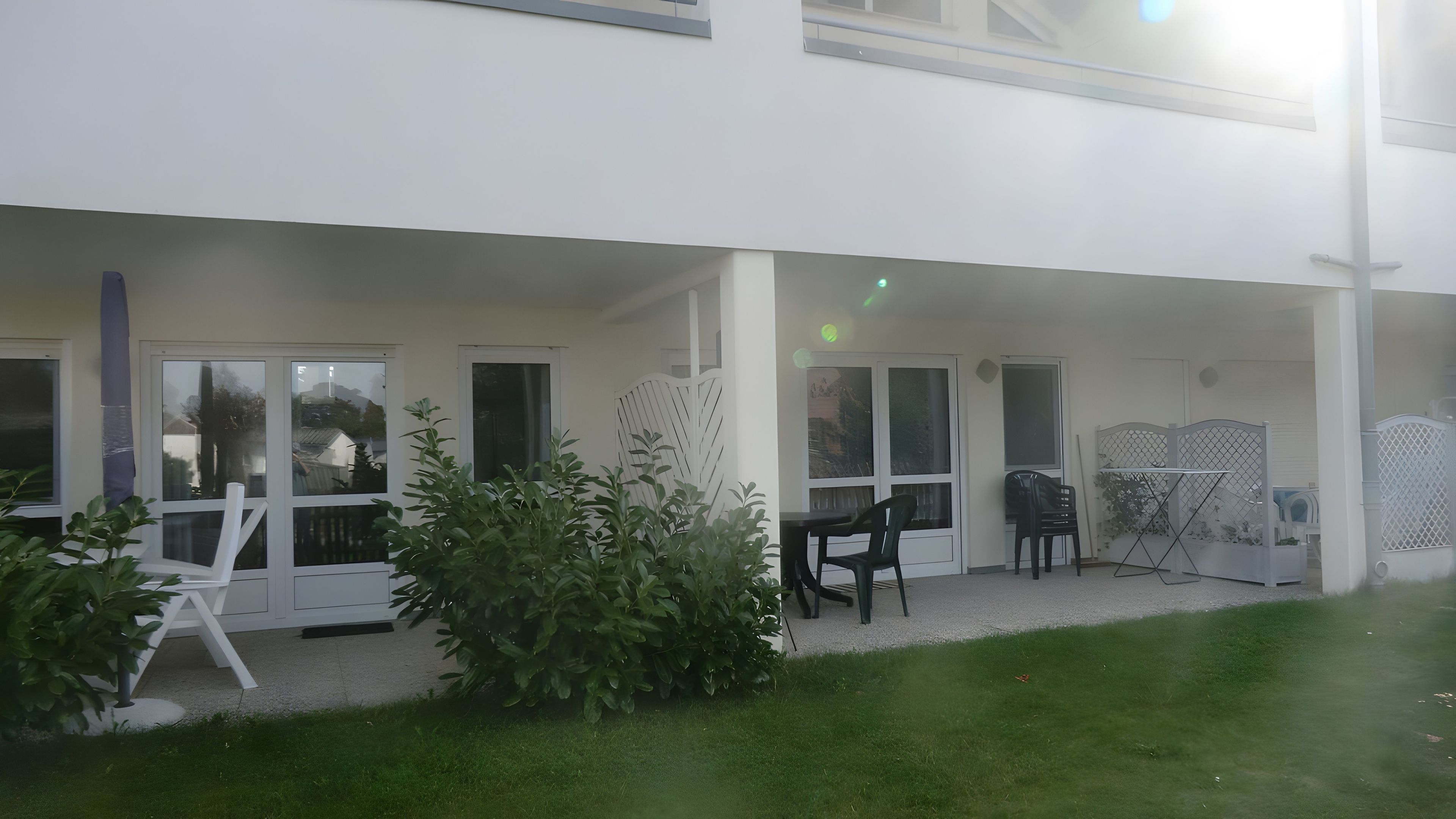 Un espace extérieur abrité, aménagé avec des sièges, un petit jardin et un bâtiment doté de nombreuses fenêtres.