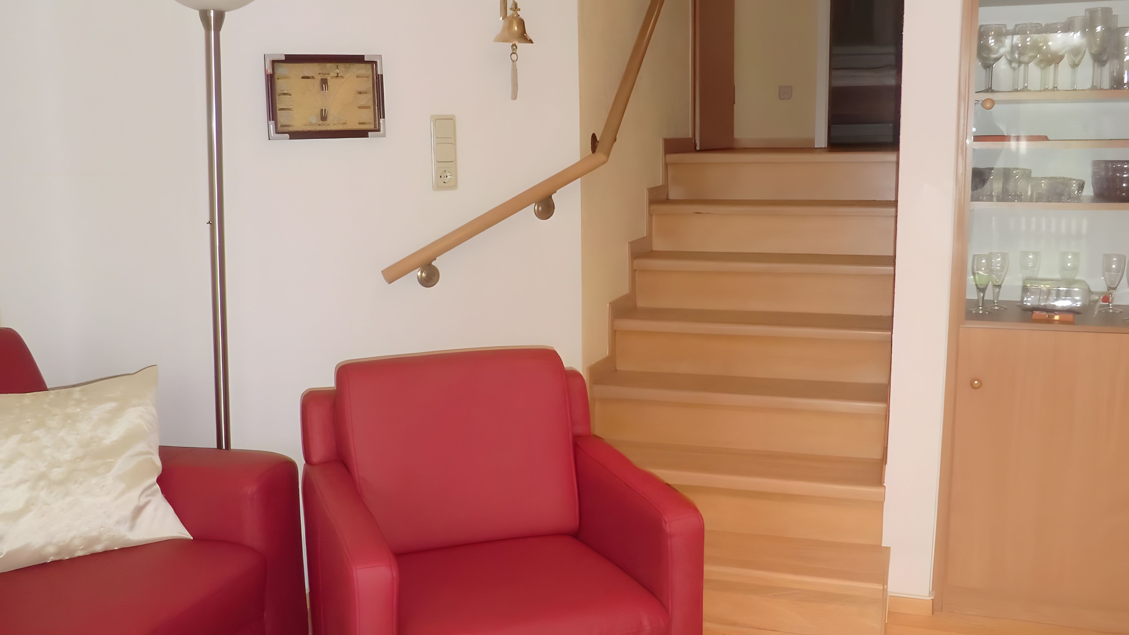 Un escalier avec une rampe en bois et une chaise rouge au premier plan.