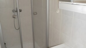 Un box de ducha con puerta de vidrio, pared con azulejos blancos y encimera blanca.