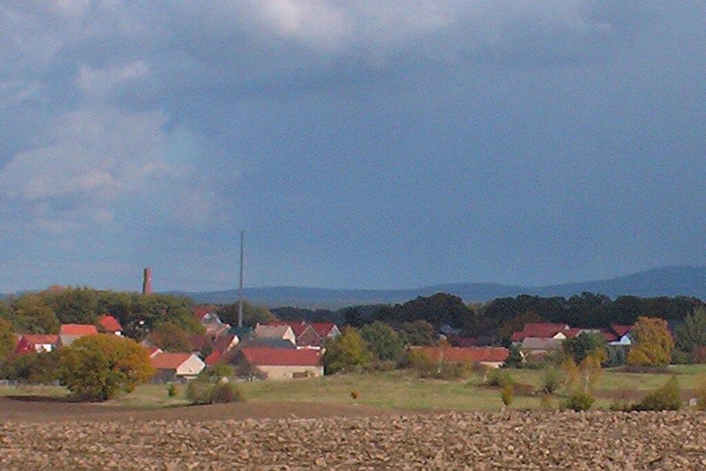 Ländliche Landschaft mit Häusern, blauem Himmel und fernen Bergen.